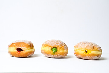 Side view of three bomboloni doughnut with strawberry, pineapple and matcha filling isolated on white background. clipping path. homemade. Italian stuffed donuts. close up.