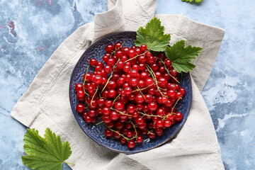 Plate with fresh red currants and leaves on blue background