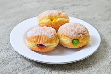 Close up view of three bomboloni doughnut with strawberry, pineapple and matcha filling on white plate. homemade. Italian stuffed donuts. grey or gray cement on the background.