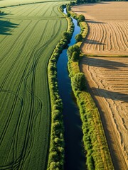 Bird’s-eye view of a narrow river splitting an agricultural landscape, green crop fields on one side and dry hayfields on the other