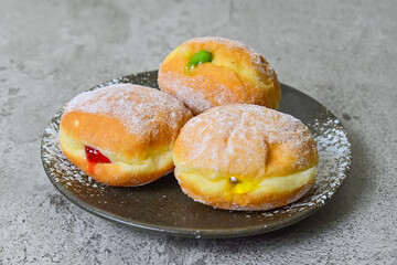 Close up view of three bomboloni doughnut with strawberry, pineapple and matcha filling on black And white plate. homemade. Italian stuffed donuts. grey or gray cement on the background.