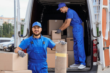 Male mover unloading boxes and rolled carpet on street