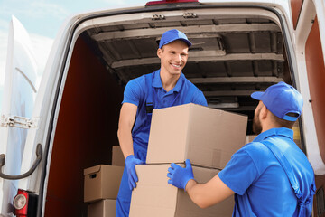 Male movers unloading car with boxes on street