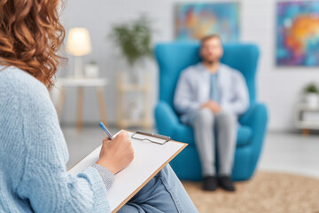 Psychologist taking notes during therapy session with male patient