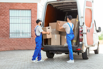 Male movers unloading car with boxes on street, back view