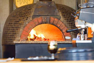 Traditional Wood-Fired Brick Pizza Oven in Restaurant Interior. Close-up of a traditional wood-fired brick oven with a burning flame inside, located in a cozy restaurant kitchen.