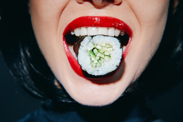 Close-up of a woman with vibrant red lips holding sushi in her mouth, showcasing a bold culinary experience.