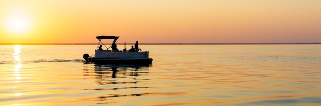 Enjoy a serene sunset fishing scene on the Baltic Sea. A gentle pontoon boat carries fishermen, capturing the beauty of nature and the tranquility of marine recreation.