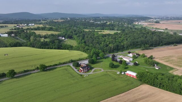 Idyllic and calm city suburb ich farm house and car on intersection. Rural area of America town with farm fields and large properties. Aerial rising wide shot. Summer season footage.
