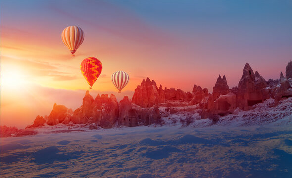 Hot air balloon flying over spectacular Cappadocia - Rock formation in Cappadocia following a heavy snow fall. Everything covered snow under sunset  sky - Powered by Adobe