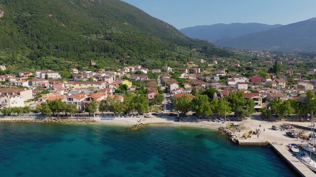 Aerial pullback shot reveals Sami town and port surrounded by turquoise sea, hills and mountains covered in pine trees, Kefalonia Island