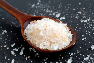 On a black background lies a wooden spoon with pink sea salt.