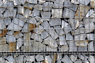 An unusual fence made of granite fragments folded into a checkered iron box.	