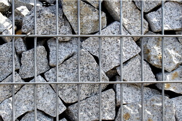 An unusual fence made of granite fragments folded into a checkered iron box.	