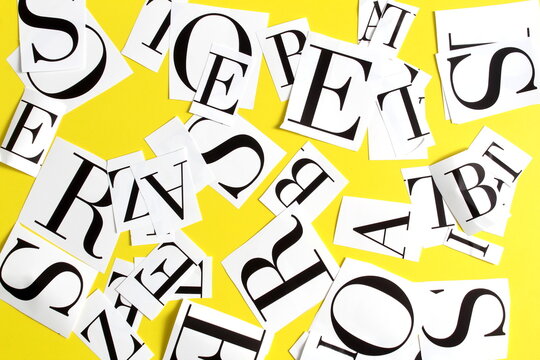 On a yellow background there are English letters cut out on paper. - Powered by Adobe