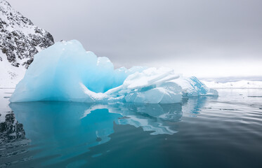 Blue iceberg from a glacier with reflection before a storm drifting in the ocean around Svalbard, Norway
