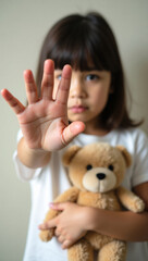 A Child's Stop Sign: A young girl holding a teddy bear, holding out her hand to show stop with her little hands. A moment of seriousness with a touch of vulnerability