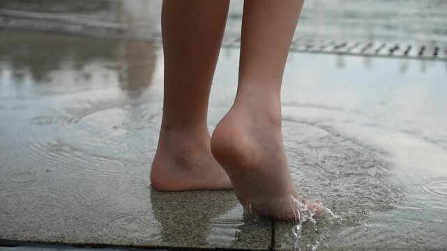 Close-up of a child's bare feet making circular motions with a toe in fountain water on paving slabs