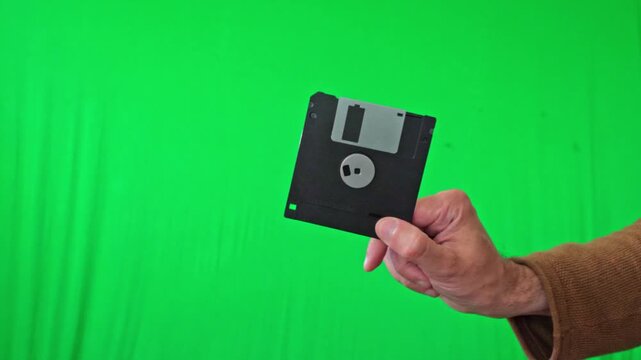 A nostalgic and technical mood is captured as a hand holds a classic 3.5-inch floppy disk, ready for integration into various digital or historical themes against a vibrant green screen