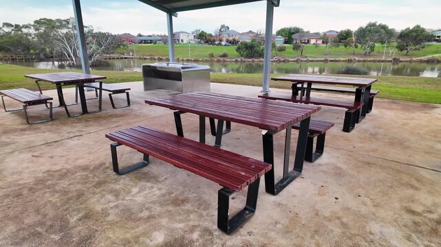 Picnic tables, benches, and a public barbecue station overlooking the lake at Navan Park, Melton, Melbourne, Australia. Suburban green space for family outings, outdoor dining, community recreation