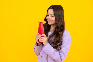 Teen child girl with shampoo bottle or shower gel isolated on yellow background. Kids hair cosmetic product. Happy teenager, positive and smiling emotions of teen girl.