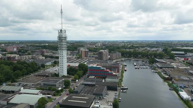 Detailed drone view circling a modern telecom tower in Alphen aan den Rijn with surrounding buildings and marina.