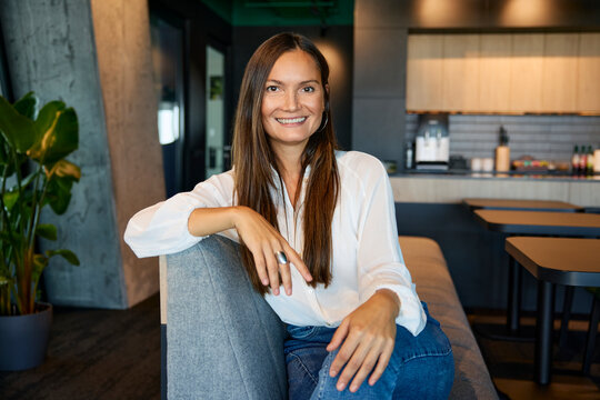 Smiling businesswoman sitting on sofa in office cafeteria