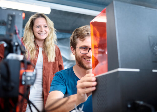 Smiling engineer assembling SLA printer with colleague at workshop