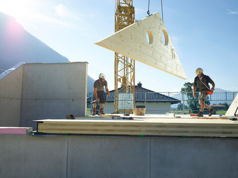 Carpenters with crane working on rooftop at construction site