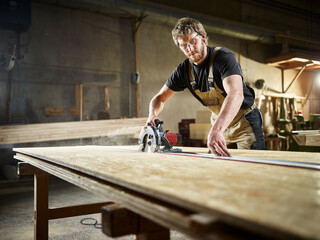 Carpenter cutting oriented strand board with circular saw in workshop