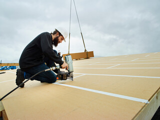 Carpenter using nail tool on wooden rooftop