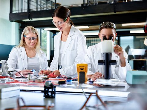 Engineer teaching trainee with colleague looking through microscope
