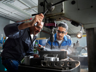Instructor with trainee spraying lubricant on drill bit at workshop