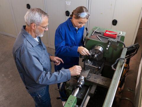 Instructor educating trainee using lathe machine at workshop