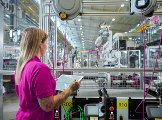 Technician with tablet PC operating and examining machinery in factory