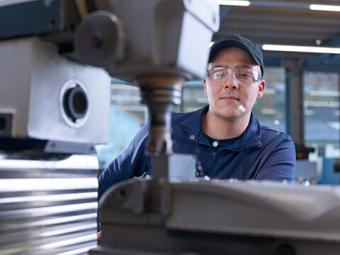 Engineer wearing cap working with CNC machine at factory