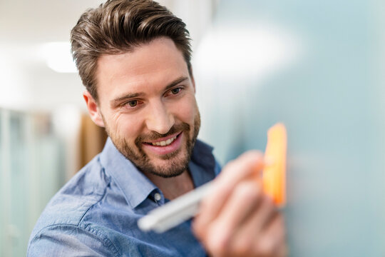 Smiling businessman writing on adhesive note in office