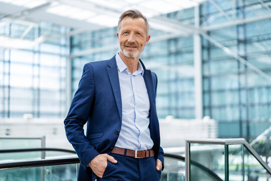 Confident mature businessman with hands in pockets by railing