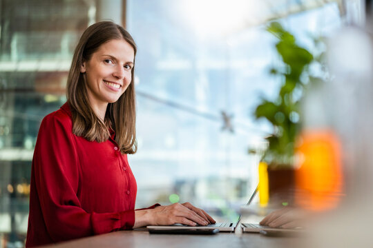 Smiling businesswoman with laptop on desk at work place