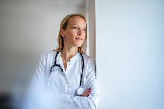 Pensive female doctor leaning against a wall
