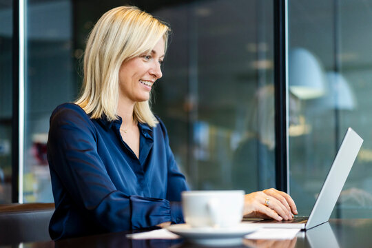 Smiling freelancer working on laptop sitting at cafe