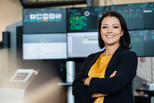 Smiling businesswoman with arms crossed in front of computer monitors