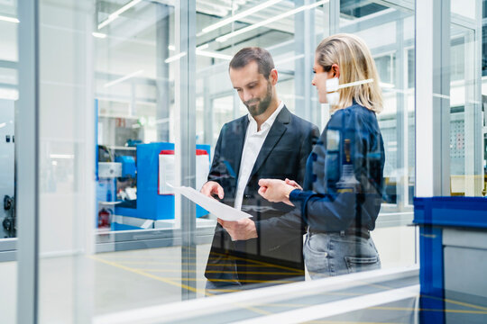 Businessman reviewing documents with colleague in factory seen through glass