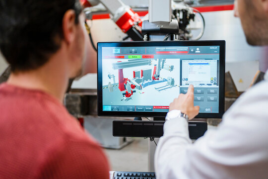 Technician pointing on computer screen with colleague at robot factory