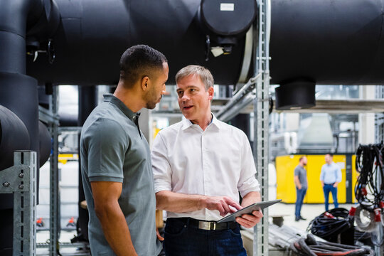 Employee and businessman with digital tablet talking in factory