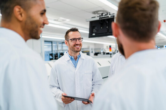 Team of competent electrical technicians in lab coats having meeting in electronics factory