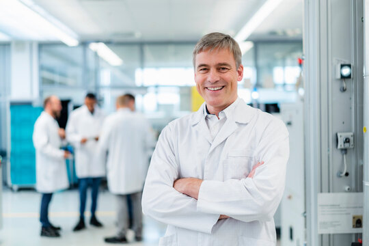Technician in white lab coat standing in electronics factory with arms crossed