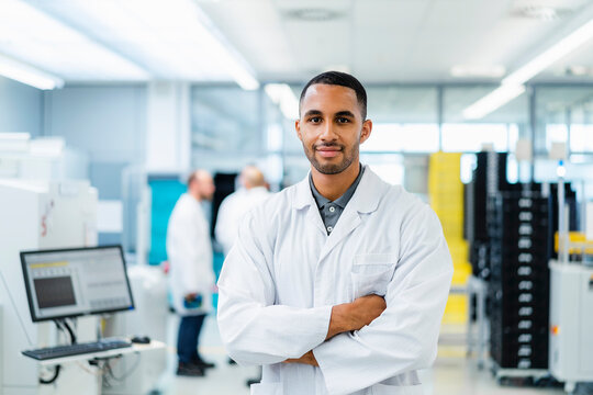 Confident technician smiling with arms crossed while colleagues are talking in electronics factory