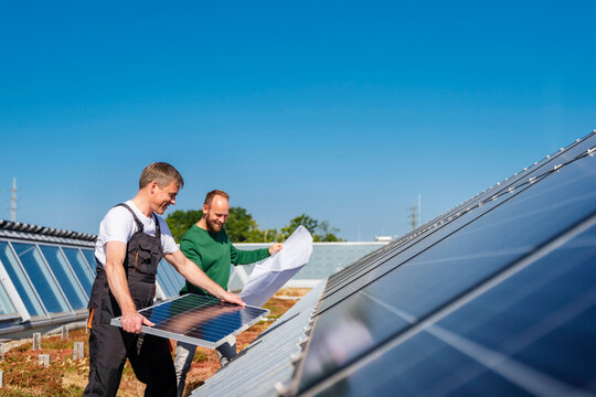 Craftsman installing solar panel on the roof of a company building with colleague holding plan
