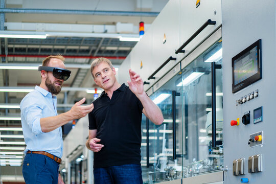 Technician wearing augmented reality glasses in a factory interacting with colleague